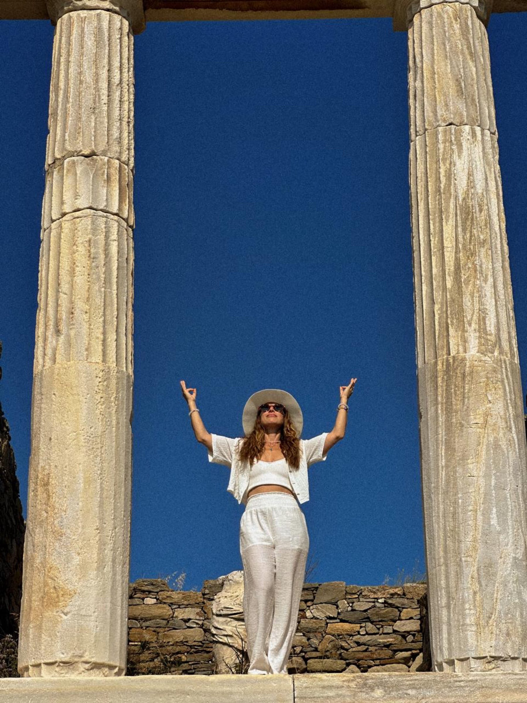 Arms raised between two old columns under a blue sky