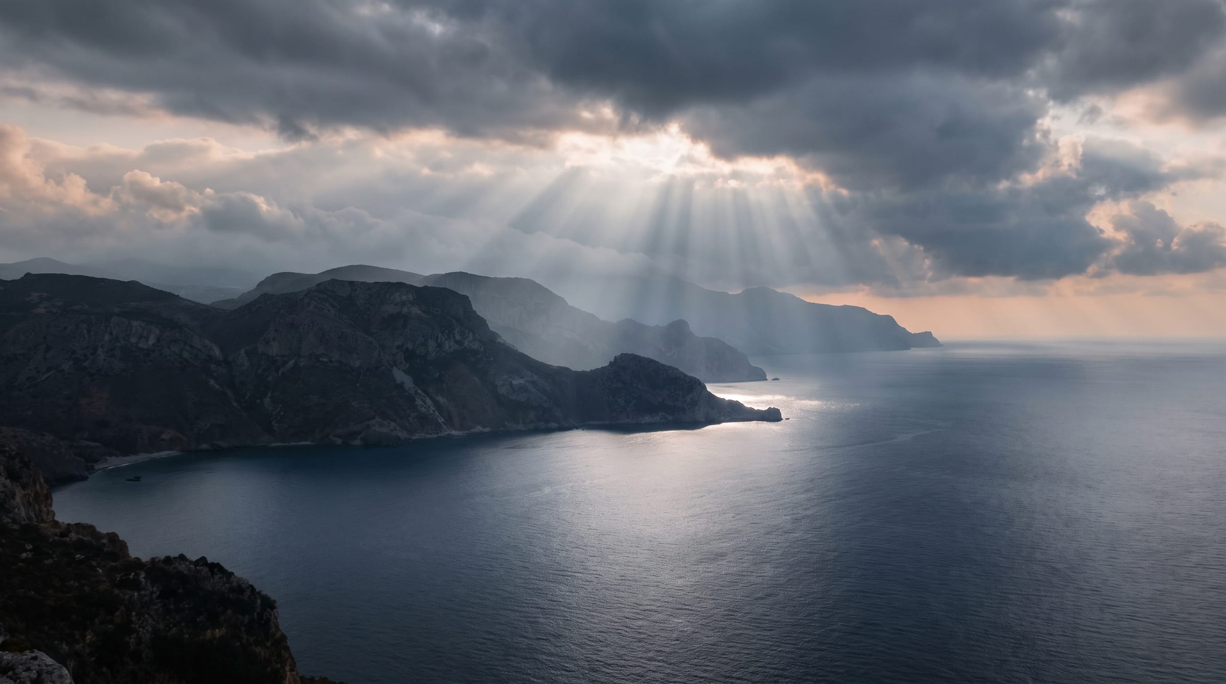 Sunbeams breaking through storm cloud over dark headlands and a silver sea